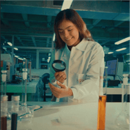 Mujer en laboratorio con una lupa examinando un frasco para campaña públicitaria hecha por Dreamerz Club